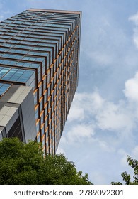 A low angle view looking up at a tall, modern glass skyscraper building reaching into a cloudy blue sky. The image symbolizes architectural strength, corporate ambition, financial growth, and modern engineering.