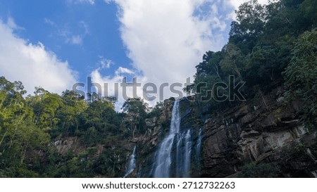 Low angle view looking up at the waterfall against a blue sky. The perspective creates a sense of awe and emphasizes the height of the natural wonder.