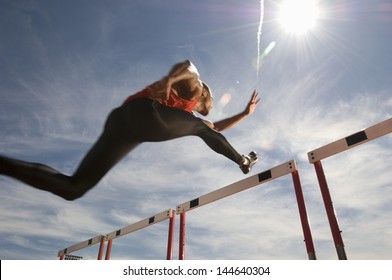 Low angle view of a male athlete jumping hurdle against the sky