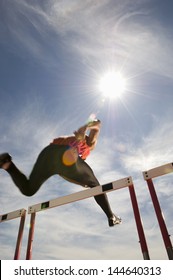 Low Angle View Of A Male Athlete Jumping Hurdle Against The Sky