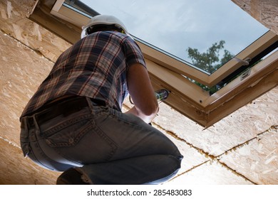 Low Angle View Of Male Construction Worker Builder Applying Fresh Caulking To Sky Light In Ceiling Of Unfinished Home