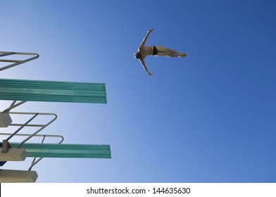 Low angle view of a male swimmer preparing to dive from diving board against clear blue sky
