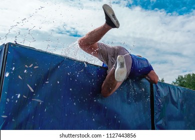 Low angle view of man getting out of the water obstacle against sky during an extreme mud obstacle race. Rear view. - Powered by Shutterstock