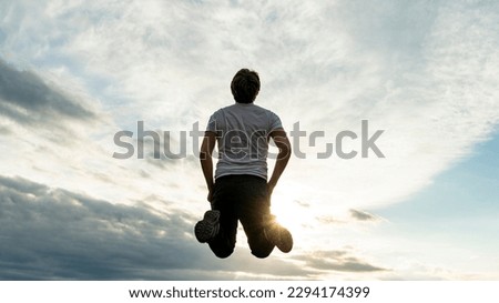 Low angle view of a man jumping up high in the air under a dramatic sky in a conceptual image of life, celebration and spirituality.