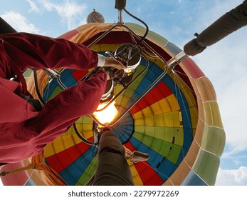 Low angle view - man operating hot air balloon, giving it a boost in flight