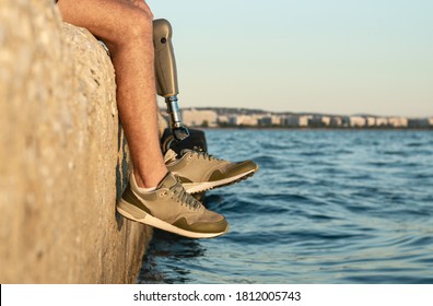 Low angle view at man with prosthetic leg sitting near the sea. Selective focus - Powered by Shutterstock