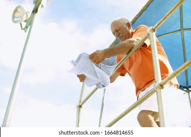 Low angle view of man reading a newspaper while leaning on metal bar