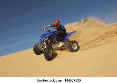 Low angle view of a man riding quad bike in desert against the blue sky