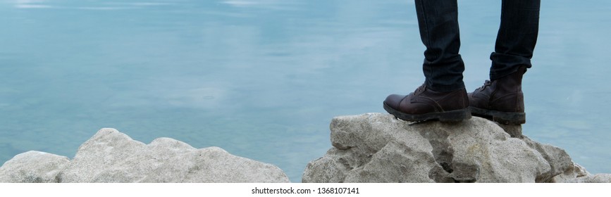 Low angle view of man standing on the rocky cliff, water background.