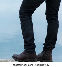 Low angle view of man standing on the rocky cliff, water background.