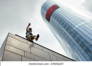 Low angle view of man in stylish clothes walking on the edge of modern building wearing VR glasses with head-mounted display, obsessed with augmented reality, moving carelessly, almost falling down