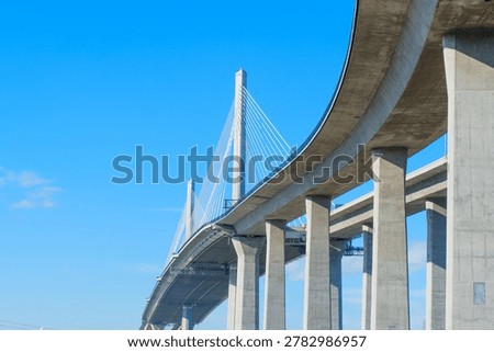 Low angle view of massive concrete pillars and cable-stayed design of the Long Beach International Gateway Bridge under a clear blue sky in Los Angeles harbor area, California.