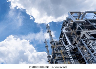Low angle view of massive distillation towers and complex pipeline systems at an oil refinery under a bright blue sky