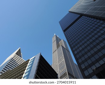 Low angle view of the massive Willis Tower framed by angular, dark glass and white contemporary buildings.
