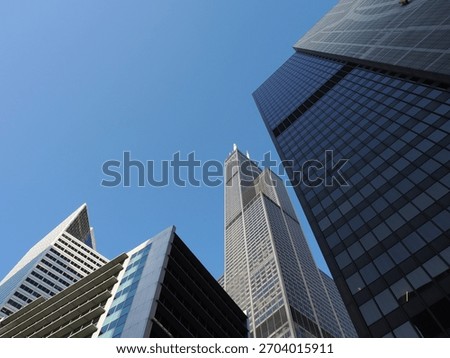 Low angle view of the massive Willis Tower framed by angular, dark glass and white contemporary buildings.
