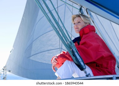 Low Angle View Of A Mature Woman In Red Jacket Sitting On The Deck Of The Sailing Boat Below Sail.