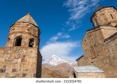 Low angle view of medieval Gergeti Trinity Church located against cloudy blue sky on sunny day in highlands of Georgia