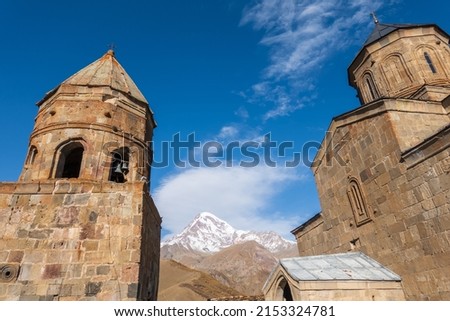 Low angle view of medieval Gergeti Trinity Church located against cloudy blue sky on sunny day in highlands of Georgia