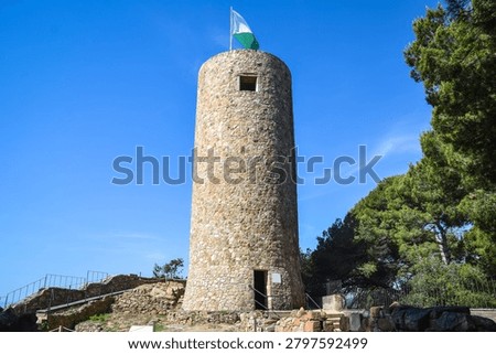Low angle view of the medieval stone tower at Castell de Sant Joan fortress against a blue sky, Lloret de Mar, Costa Brava, Spain.