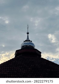 A low angle view of a metallic dome pinnacle against a cloudy sky, showcasing architectural details of a structure.