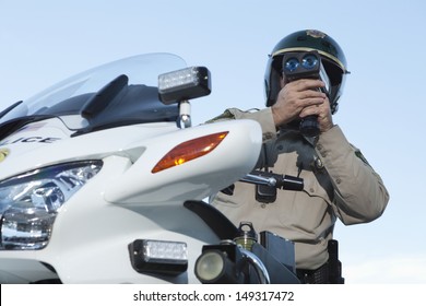 Low angle view of middle aged policeman monitoring speed through radar against sky
