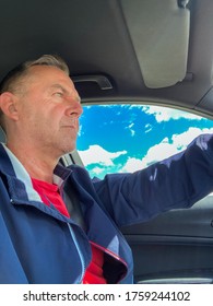 Low angle view of an middle aged man driving a car on summer road. Inside view
