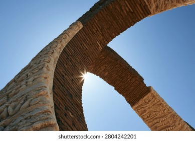 Low angle view of a modern architectural structure with sunlight peeking through the arch.