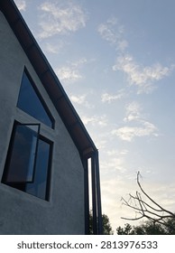 Low angle view of a modern building facade with unfinished concrete walls and an open geometric glass window against a bright blue sky with scattered clouds. Minimalist architecture background.