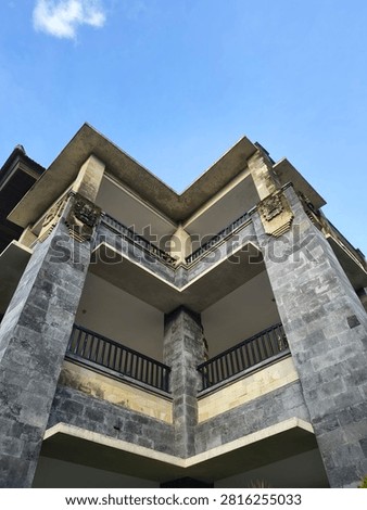 Low angle view of a modern building with stone pillars and traditional Balinese architectural ornaments against a clear blue sky