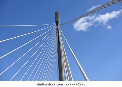 Low angle view of a modern cable-stayed bridge pylon with radiating steel cables against a clear blue sky, emphasizing geometric patterns, engineering design, and architectural minimalism