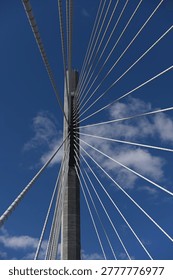 Low angle view of a modern cable-stayed bridge pylon with radiating steel cables against a clear blue sky, emphasizing geometric patterns, engineering design, and architectural minimalism