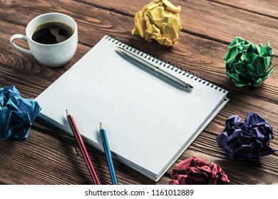 Low angle view of modern creative workplace with notepad, pencils, crumpled paper balls and coffee on wooden table.