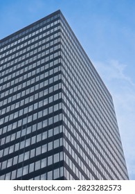 Low angle view of a modern dark glass skyscraper facade with grid windows against a blue sky.