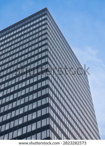 Low angle view of a modern dark glass skyscraper facade with grid windows against a blue sky.