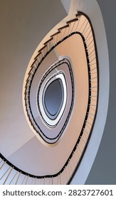 Low angle view of a modern elegant oval spiral staircase with an abstract architectural background. This mesmerizing bottom-up perspective captures a contemporary elliptical staircase, highlighting its striking geometric symmetry, clean lines, and smooth, sweeping curves that form a captivating white vortex. The soft pastel tones and minimalist aesthetic showcase elegant interior design, creating a powerful sense of depth, infinity, and modern architectural luxury