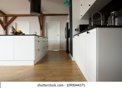 Low Angle View Of A Modern Kitchen Interior With Wooden Floor, White Cupboards And Black Countertop