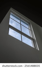 Low angle view of a modern rectangular window with clear glass panes, framing a bright blue sky with light clouds.