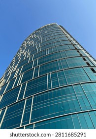 Low angle view of modern skyscraper with glass facade reaching towards clear blue sky. Symbol of ambition, growth, and corporate success.