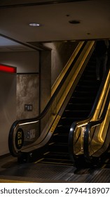 Low angle view of a modern underground subway escalator with warm golden lighting and B1 West directional signs.