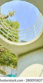 Low angle view of a modern white circular concrete structure with metal railings reaching towards a clear blue summer sky
