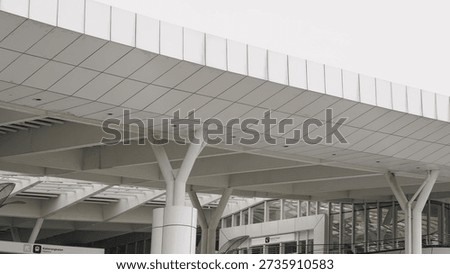 Low angle view of a modern white airport terminal exterior featuring clean geometric lines, large roof overhang, and distinctive Y-shaped structural columns. The minimal color palette and contemporary design details create a sleek, futuristic transport hub atmosphere that is perfect for themes of travel, infrastructure, architecture, and urban mobility. This image is ideal for use in airline marketing, transportation reports, architectural presentations, website headers, and editorial articles about airports and modern public buildings.