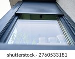 Low angle view of modern window with partially lowered roller shutter on residential house facade. Concept of home exterior, security and contemporary architecture.