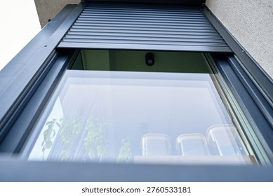 Low angle view of modern window with partially lowered roller shutter on residential house facade. Concept of home exterior, security and contemporary architecture.