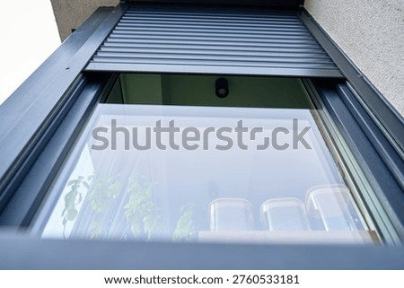 Low angle view of modern window with partially lowered roller shutter on residential house facade. Concept of home exterior, security and contemporary architecture.