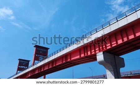 Low angle view of the monorail track structure with the iconic red Ampera Bridge under a vibrant blue sky during a sunny day