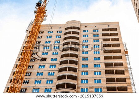 Low angle view of multi story brick building under construction with yellow crane towering beside it. Blue windows contrast warm brick tones
