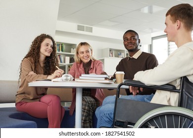 Low angle view at multi-ethnic group of students studying in college library featuring young man using wheelchair in foreground - Powered by Shutterstock