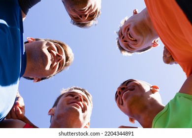 Low angle view of a multi-ethnic group of male runners training at a sports field, in a motivational huddle, with arms around shoulders, smiling in the sun against blue sky - Shutterstock ID 2204344891