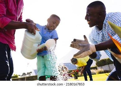 Low angle view of multiracial boy with father, grandfather watering plants against clear sky. Copy space, multigeneration, family, gardening, nature, unaltered, together, childhood, retirement, yard. - Powered by Shutterstock