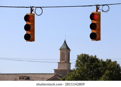 Low angle view of municipal traffic light signals suspended on overhead utility wires over a small town intersection crossroad.